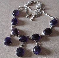 Top view of the necklace laid out, showing the oval dark purple amethyst stones and three dangling cabochons.