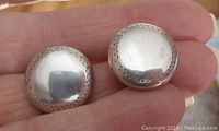 Close-up photo of front of earrings held in hand showing round shape, smooth polished center, and engraved edge detail.