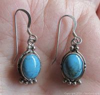 Front view of the pair of turquoise oval cabochon earrings held in the palm showing the stone and silver bead accents