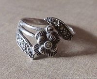 Close-up photo of vintage sterling silver flower ring showing detailed flower and leaf design with marcasite stones, on a plain background.
