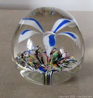 Front view of the paperweight showing the flower design inside with blue and white petals and multicolor base.