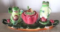 Front angle of hand painted frog condiment set showing two frogs on a leaf base with central flower container topped with bee decoration.