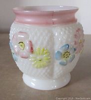 Side view of antique milk glass spoon holder showing the white lattice textured body with yellow, pink, and blue pastel flowers and soft pink rim.
