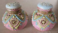 Pair of antique Nippon porcelain shakers viewed from the side, showing detailed Moriage and beaded decoration in pink, blue, and multicolor.