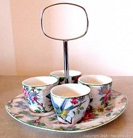 Front view of four egg cups with birds and rose pattern on square floral tray with metal handle