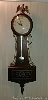 Full view of the electric wooden wall clock with eagle finial and visible pendulum.