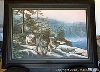 Full view of framed wolf picture showing three wolves on rocky landscape with forest and river scenery