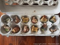 Top-down view of 12 small vintage animal tea figurines inside an egg carton, showing all items clearly.