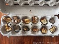 Twelve small vintage ceramic animal and scene figurines placed in an egg carton, showing details and condition.