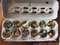 Photo of 12 vintage tea figurines displayed in egg carton, showcasing various animal and human character designs in good condition