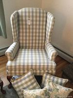 Full view of plaid wingback armchair with throw pillows in front