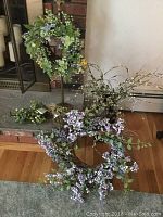 Image showing two floral wreaths and a faux floral garland on a wooden floor and near a fireplace.