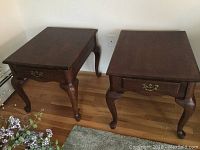 Two dark hardwood end tables with cabriole legs and single drawer with brass handle seen from angled top view.