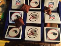 Close-up image of Toss Across game squares with New England Patriots and NFL logos and brown bean bags on top.