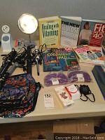 Photo showing curling irons, cosmetic tote bags, health and fitness books, hand weights, magnifying mirrors, and other accessories arranged on a table.