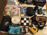 Lot overview showing children's audiobooks, DVDs, electronic gadgets like joystick, Walkman, rubber keyboard, computer mouse, DVDs, and accessories.