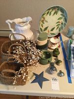 Photo showing two wicker baskets, white ceramic water jug and wash bowl, Chinese decorative plate with painted floral and bird design, Royal Albert teacup and saucer, four bird figurines, four small stacking boxes, and a blue star decoration on a table.