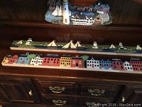 Decorative wooden nautical village plaques with houses and sailboats displayed on a wooden cabinet surface