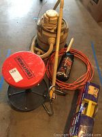 Wide view showing Genie JetVac vacuum, Craftsman rolling stool, orange extension cord, and American Tool Group rotary laser level box on floor.