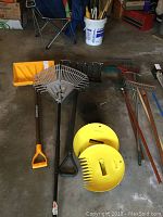 Wide shot showing multiple garden tools on floor including snow shovels, rakes, chimney brush.