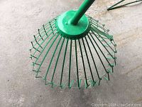 Close-up image showing the green metal rake head with circular fan-like design and multiple tines.