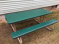 Green folding metal picnic table with attached benches shown outdoors on grass near a house.