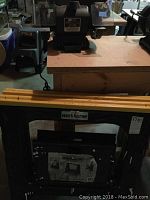 Craftsman bench grinder positioned on a wooden workbench with two black Workhorse foldable sawhorses in front.