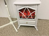 White electric portable heater with fireplace effect lit showing simulated red glowing logs behind a decorative window panel, standing on short decorative legs.