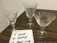 Etched clear glass wine, water and fruit glasses on table with handwritten note detailing quantities (11 wine, 12 water, 12 fruit cups).
