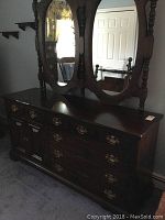 Full view of wood dresser with double oval mirrors in a room.