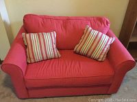 Front view of red sleeper loveseat with two striped throw pillows, showing cushioned seating and curved armrests.