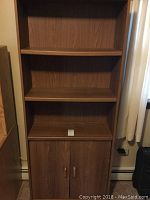 Front view of the woodgrain shelving cupboard showing two doors at the base and three open shelves above.