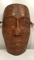 Front view of two-toned brown ceramic mask showing carved Native American facial patterns and design details.
