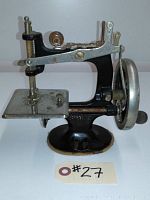 Side view of the antique miniature Singer sewing machine showing hand crank and needle plate.