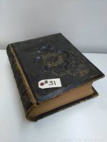 Front view of large antique German Bible with embossed black leather cover and gold lettering 'Heilige Schrift' showing wear and aged condition.