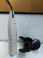 Photo of white painted wooden buoy with rope, showing wear and paint chipping, with a tag labeled #33.