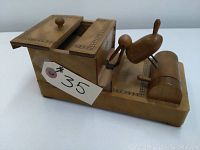 Front side view of vintage wooden cigarette box with mechanical wooden bird on rounded base attached, with sliding lid compartments on top and geometric inlay decoration.