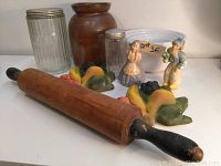 Wide view showing the wooden rolling pin, antique glazed brown pot, white mixing bowls, two vintage chalkware fruit decor pieces, and two antique Dutch chalkware figures.