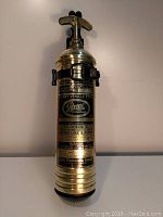 Front view of antique brass fire extinguisher showing label and pump handle.