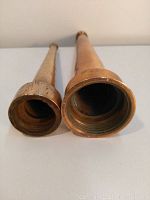 Two antique solid brass fire hose nozzles shown from the top ends, highlighting differing diameters and threading inside.