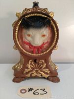 Front view of the mechanical cat and mouse coin bank showing detailed painted cat face and ornate gold and brown design.