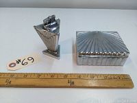 Two-piece set of chrome lighter and cigarette box placed next to a ruler for size reference.