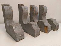 Four wooden architectural corbels standing upright showing their height and chipped gray paint surfaces with some wood exposed.