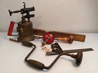 The full grouping of vintage tools showing the brass blow torch, hand drill, level, and hand brace drill.