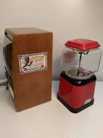 Two vintage candy dispensers side by side, showing wooden sided dispenser labeled National Druggist and the red 1 cent gumball machine.