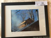 Photo of the framed photograph showing smoke from a sugar shack chimney and bare trees under blue sky