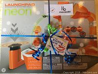 Photo of the unopened box of Hexbug Launchpad Neon interactive shooting gallery with orange and white assembly pieces shown on the package.
