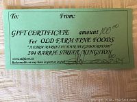 Green colored paper gift certificate with printed details about redemption at Old Farm Fine Foods, showing no expiry date and amount $100.