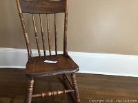 Front angle photo of the wooden antique rocking chair showing spindle back, turned legs, and wooden seat.