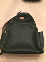 Front view of the green pebbled leather backpack showing the main compartment and front pocket with gold Michael Kors plate